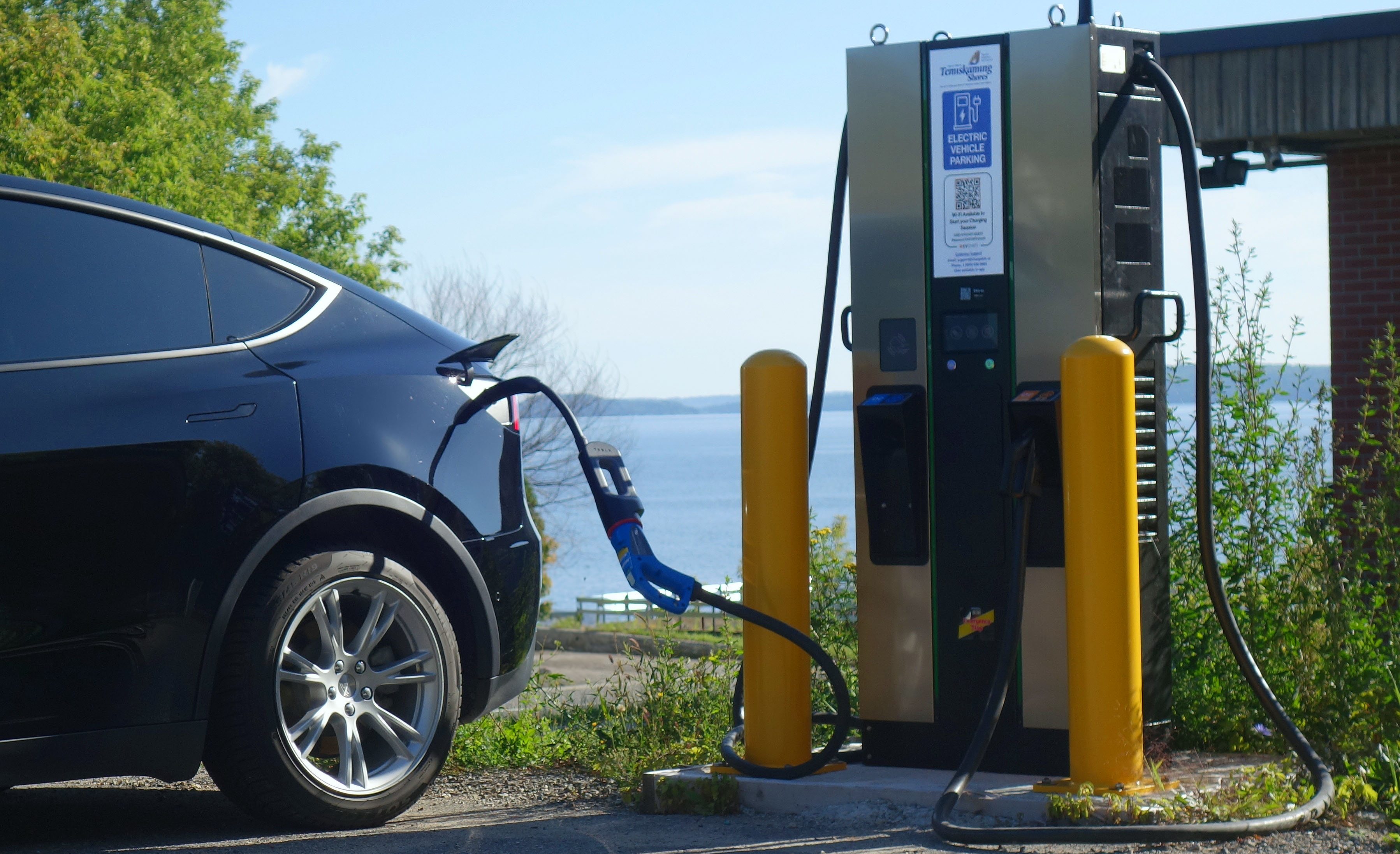 Electric vehicle charging at the Haileybury beach EVStart Charging Station in Temiskaming Shores, Ontario, with Lake Timiskaming in the background on a summer day.
